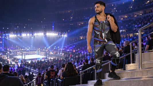 Man in a matching Cyber Riot wrestling tights and tank top set standing on arena steps before a wrestling show, jacket over his shoulder
