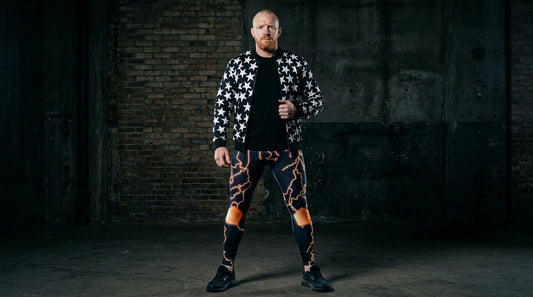 Man in Thunder Jack midnight and electric strike wrestling tights with a black bomber jacket worn open, standing against a dark cold-weather backdrop for AEW Worlds End