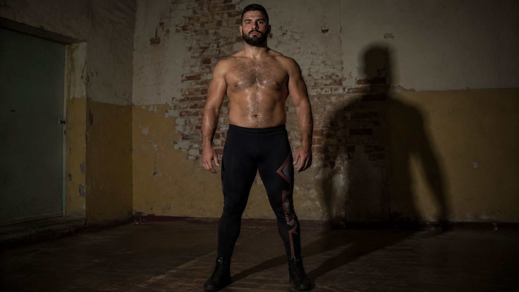 Tall stocky wrestler standing in darkened room in France