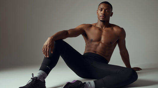 A confident adult man standing in a relaxed, neutral pose wearing plain black men’s leggings with minimal branding, no shorts layered over the top. Clean studio background in soft grey or off-white. Editorial fashion photography style.