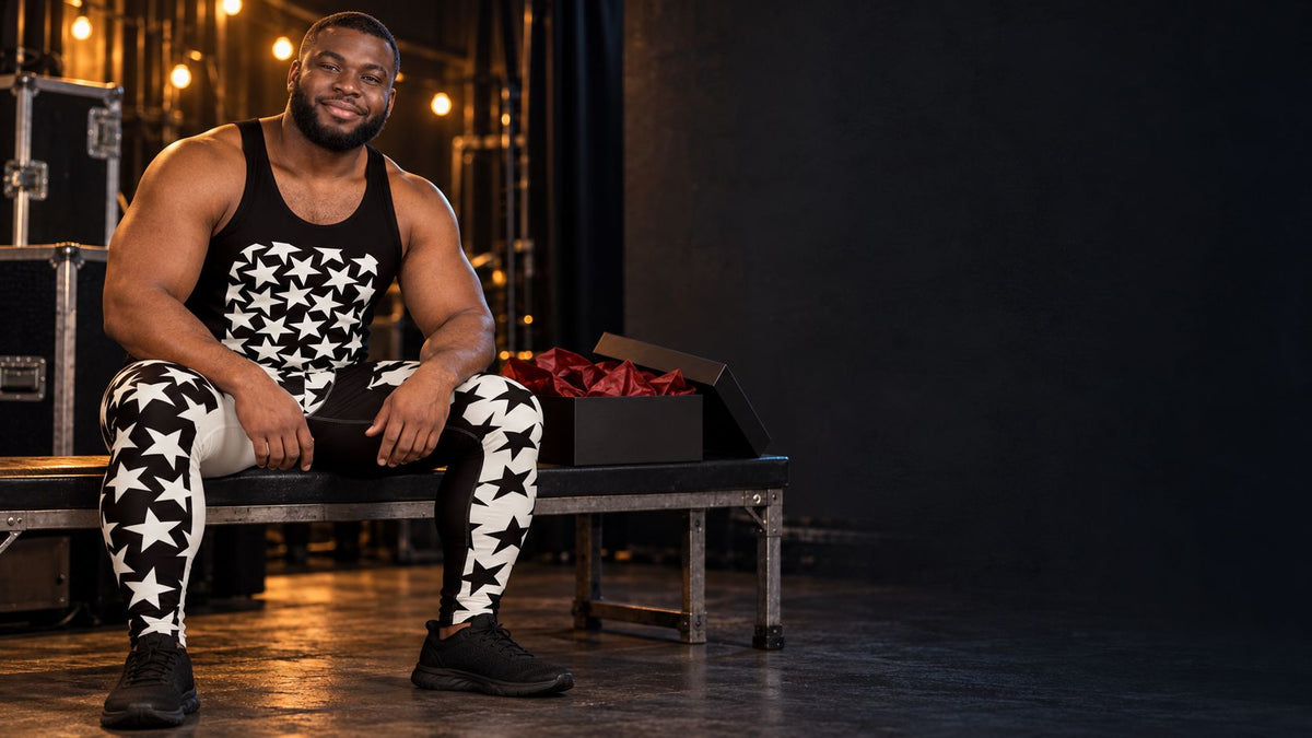 Man in black and white star print wrestling tights and matching tank top sitting backstage beside an open gift box