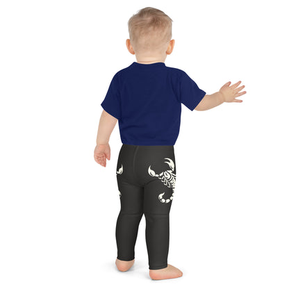 Toddler wearing dark leggings with large printed scorpion on each side, laid flat