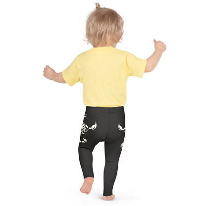Toddler wearing dark leggings with large printed scorpion on each side, laid flat
