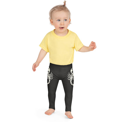 Toddler wearing dark leggings with large printed scorpion on each side, laid flat