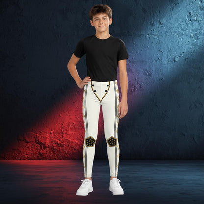 A young boy modeling white athletic cosplay wrestling tights with gold and black decorative details, paired with a black t-shirt and white sneakers, standing against a textured blue and red studio backdrop.