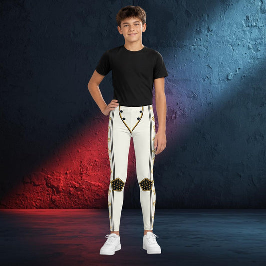 A young boy modeling white athletic cosplay wrestling tights with gold and black decorative details, paired with a black t-shirt and white sneakers, standing against a textured blue and red studio backdrop.