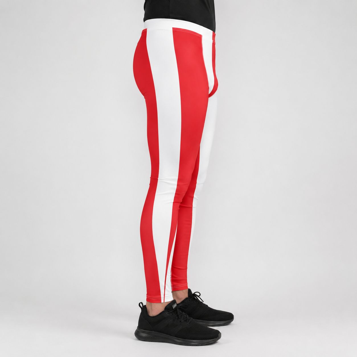 A person shown from the waist down wearing red and white striped athletic leggings with black sneakers, photographed against a light gray studio background.