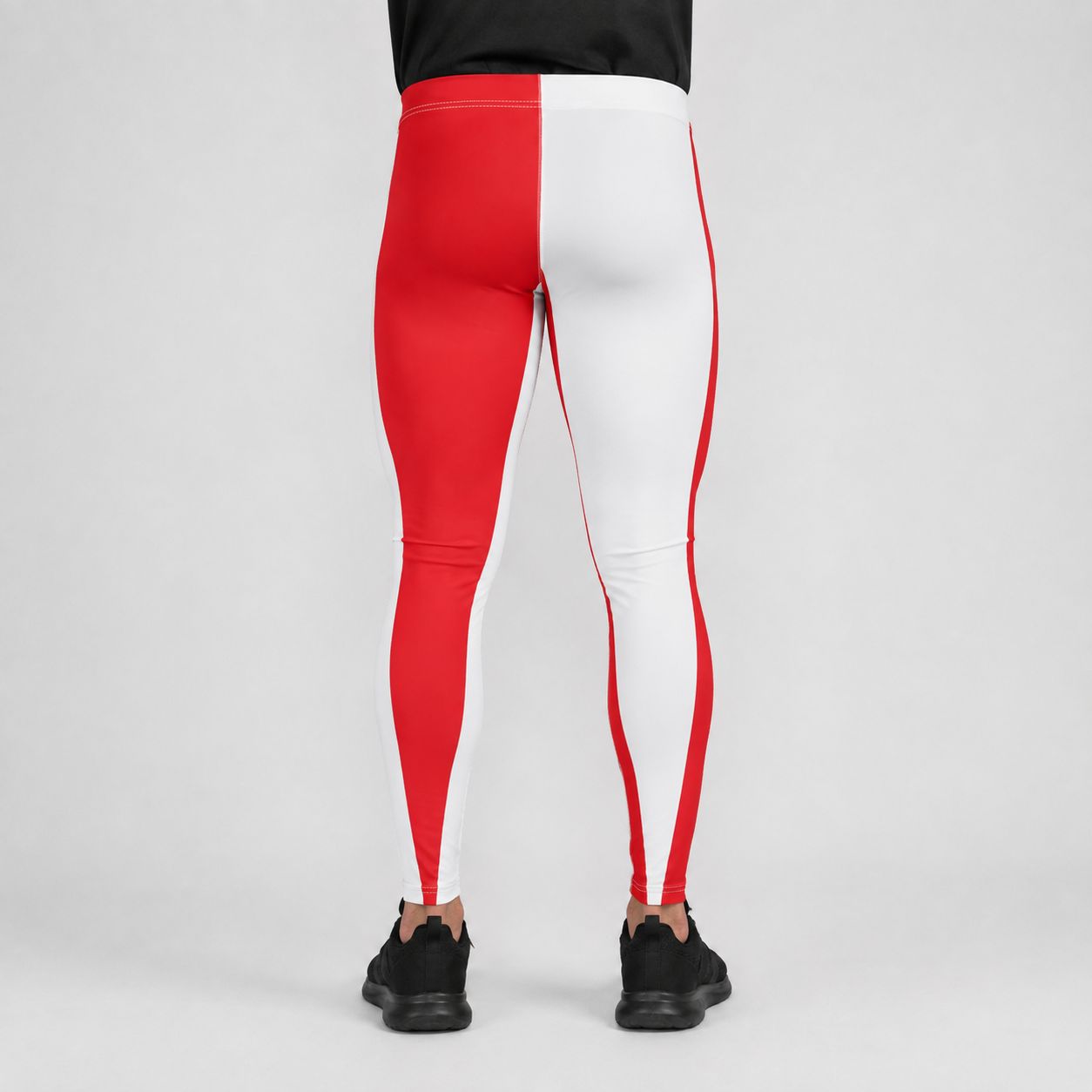 A person shown from the back wearing colorblock athletic leggings with a bold red and white split design, paired with black sneakers, against a neutral light gray studio background.