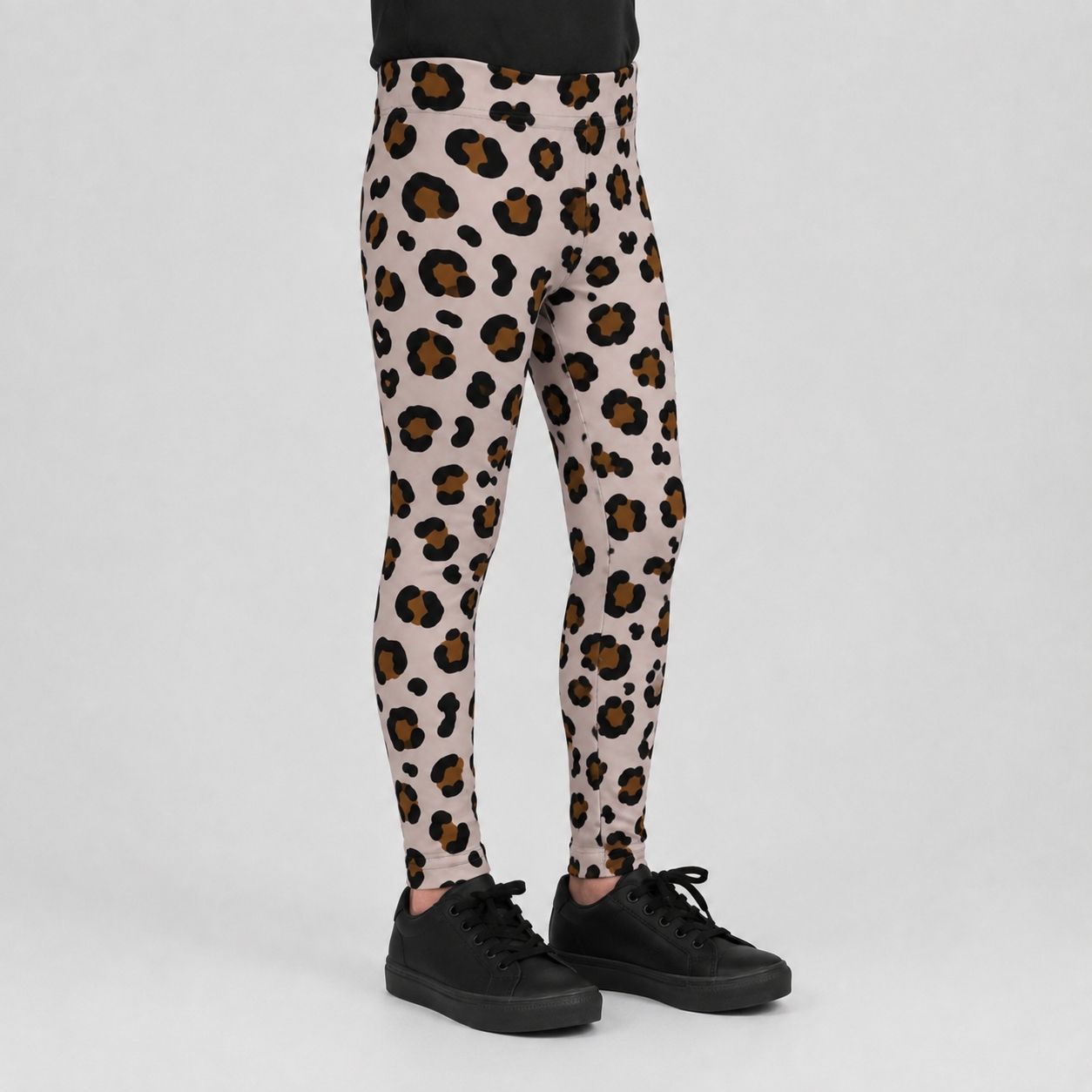 A person wearing leopard-print leggings with black sneakers, shown from the waist down against a light gray studio background.