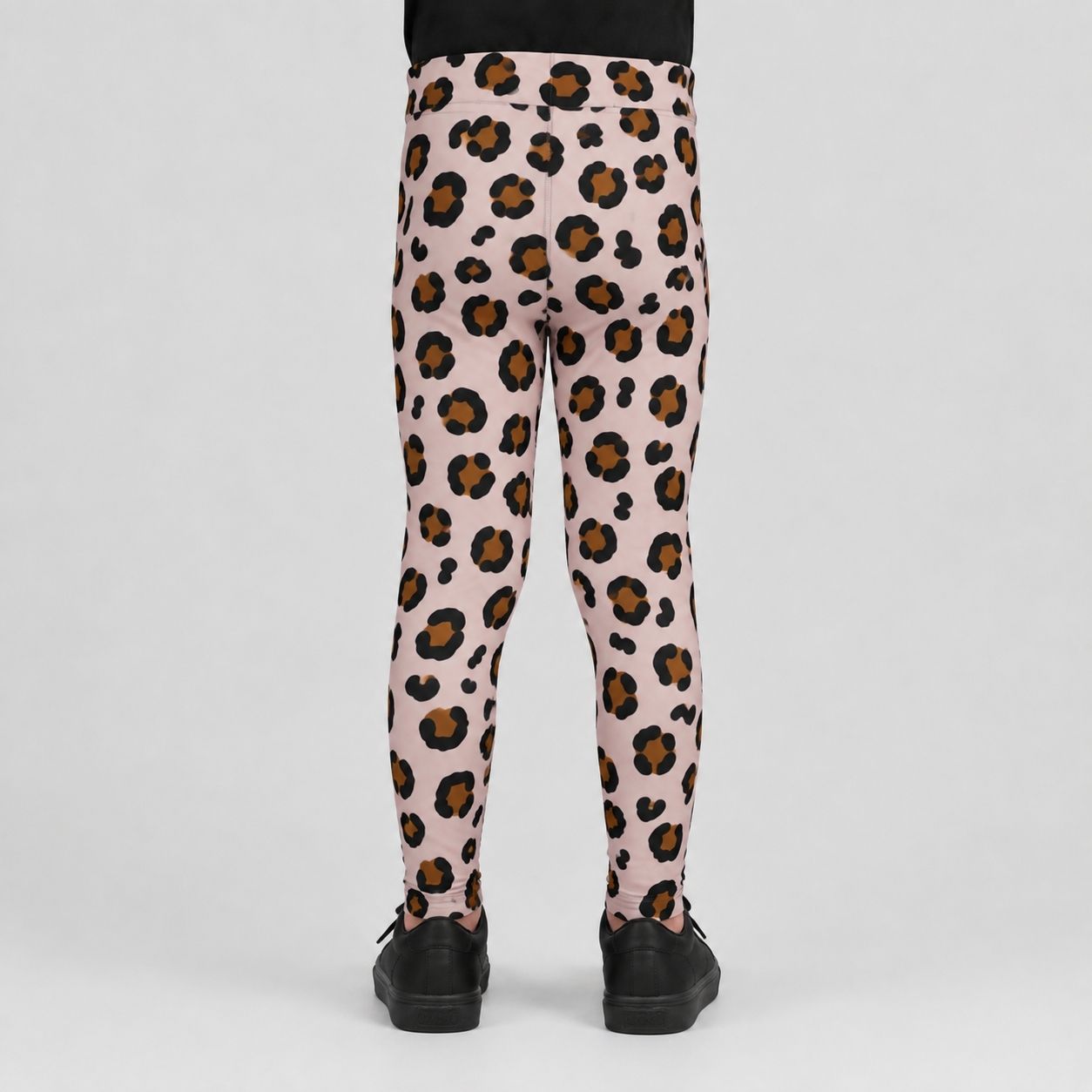 Pink leopard print leggings shown from the back on a child model, featuring a black and brown spotted pattern on a light pink base, paired with black shoes against a light gray background.