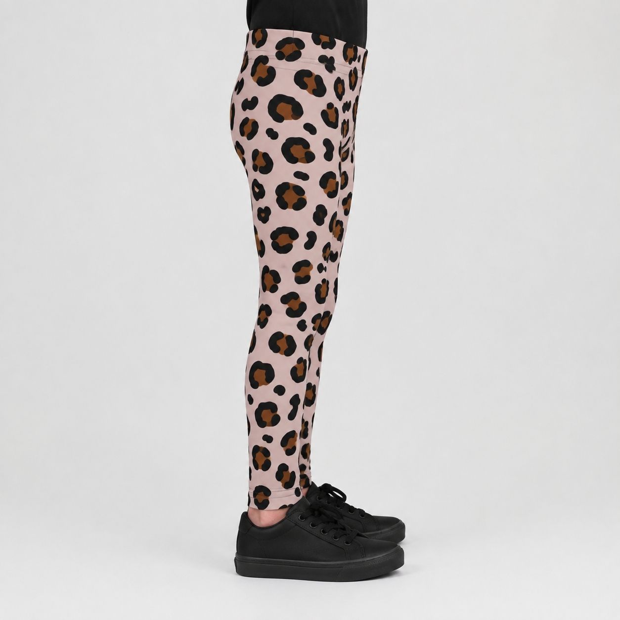 Pink leopard print leggings worn by a model, paired with black sneakers, shown from the waist down against a light gray studio background.