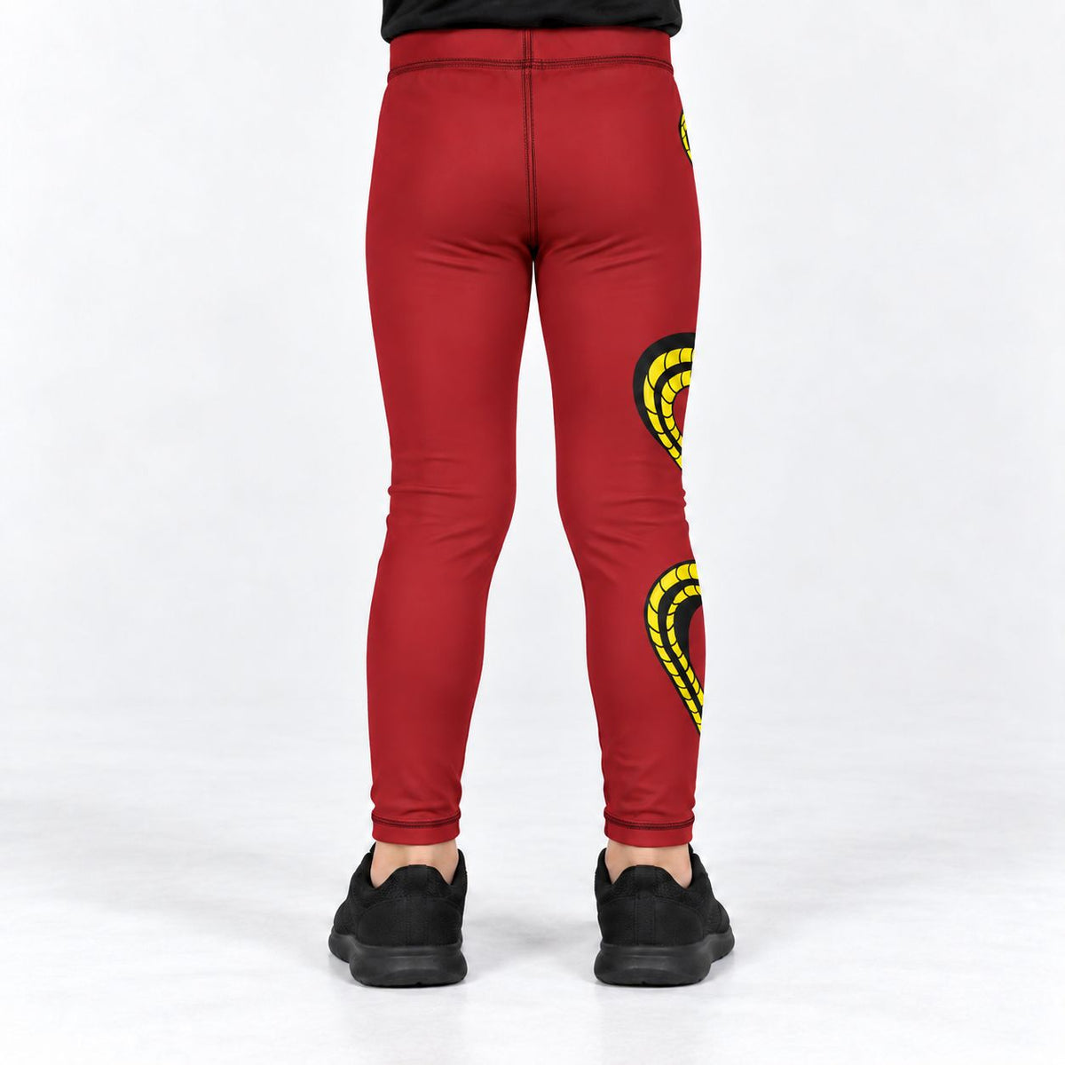 Red full-length leggings shown from the back on a model, featuring yellow and black coiled graphic designs on the upper and lower legs, paired with black sneakers against a white studio background.