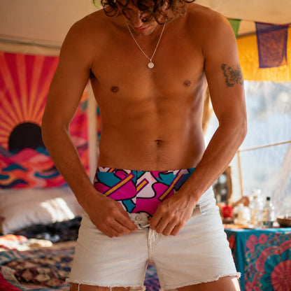 Man wearing colorful boxer shorts with a tattoo on his arm, standing in a vibrant indoor setting.