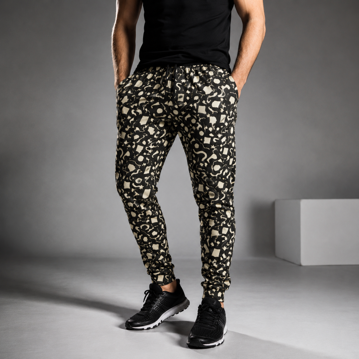 Person wearing black and beige geometric memphis patterned jogging pants on a gray background