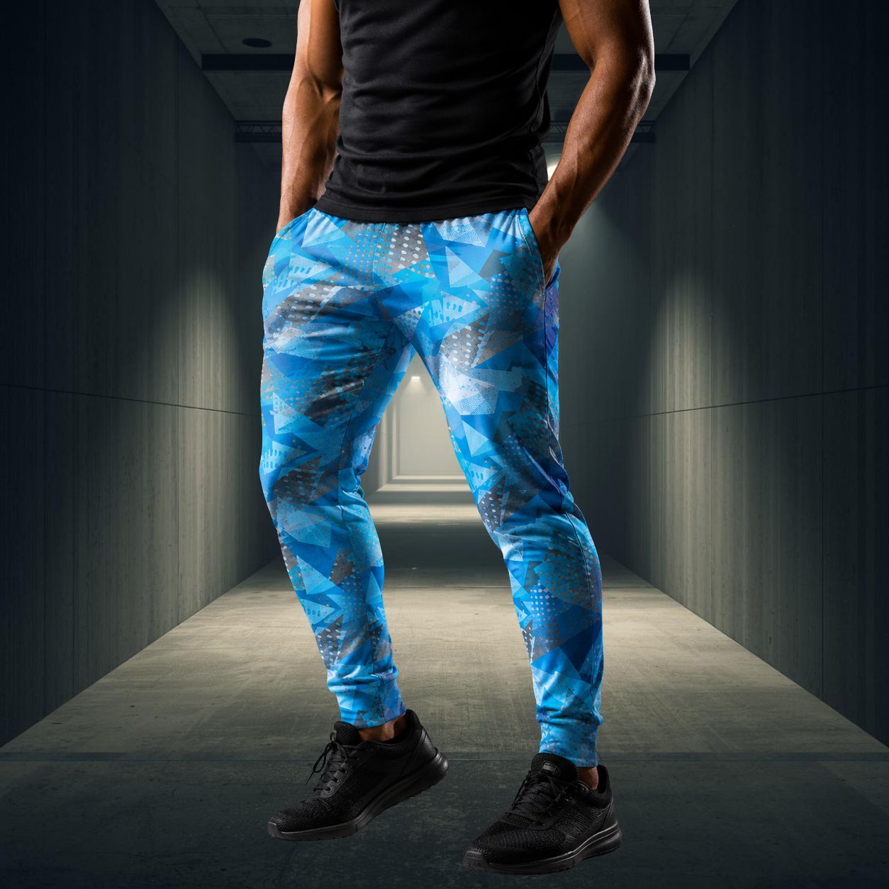 Person wearing blue patterned jogging pants and black shoes in a dimly lit hallway.