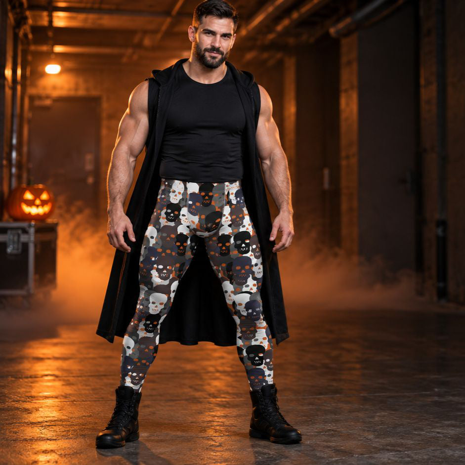 A muscular man stands in a dimly lit industrial corridor wearing patterned leggings with a black sleeveless top and a long black cape. The leggings feature a repeating Halloween-themed print of skulls, ghosts, and pumpkins in black, white, gray, and orange.