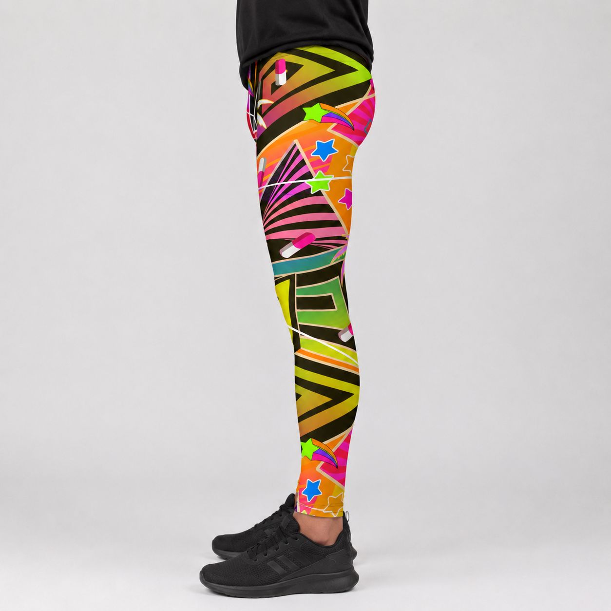 A person wearing colorful geometric patterned leggings and black sneakers, shown from the waist down against a light gray studio background.