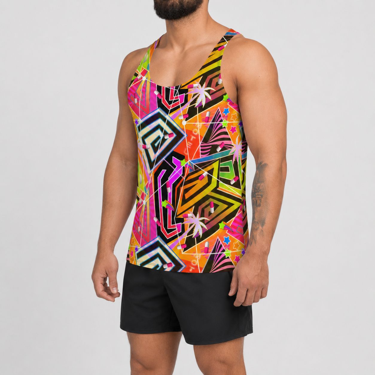 A man wearing a vibrant, multicolored geometric print rave tank top and black athletic shorts, shown from the chin down against a light gray studio background.