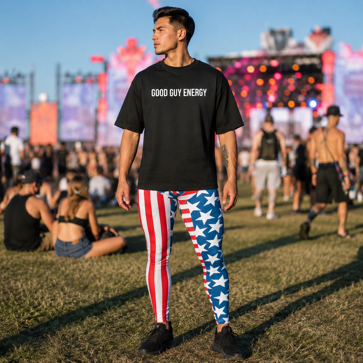Man standing at a festival wearing patriotic stars and stripes red, white and blue leggings with a black oversized t-shirt with slogan Good Guy Energy