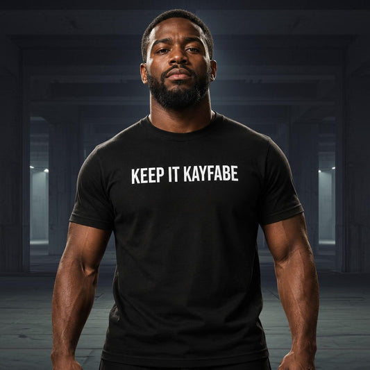 Man wearing a black t-shirt with 'KEEP IT KAYFABE' text in a dark indoor setting
