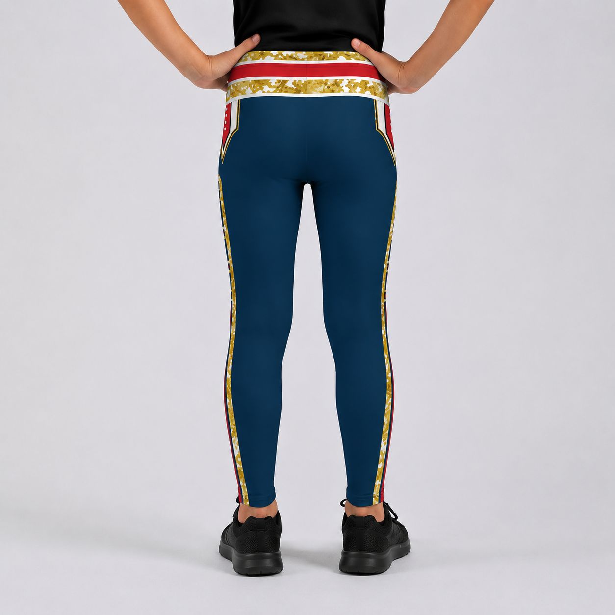 A person shown from the back wearing teal leggings with a gold and red ornate patterned waistband and side stripes, paired with black sneakers on a light gray studio background.