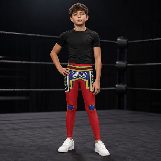 A boy stands in a boxing ring wearing a black short-sleeve athletic t-shirt and red cosplay wrestling tights in a retro American hero style with a colorful crocodile pattern on the upper thighs and blue knee patches, paired with white sneakers.