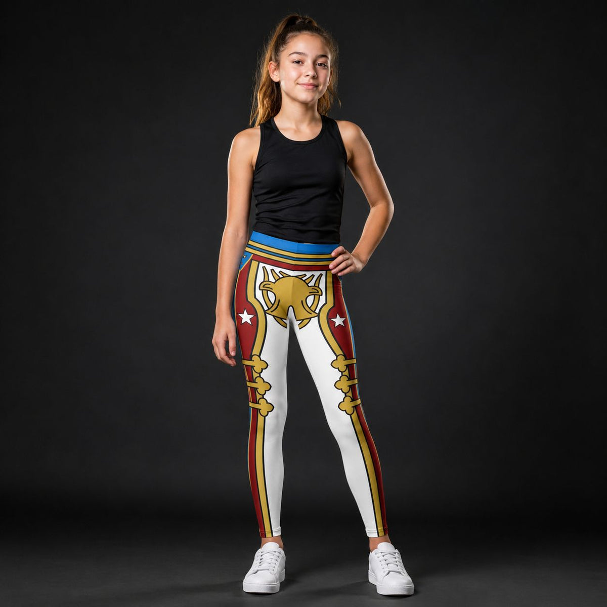 A young girl modeling a pair of white leggings with a red and gold RETRO military-style design, paired with a black tank top and white sneakers, set against a dark studio background.