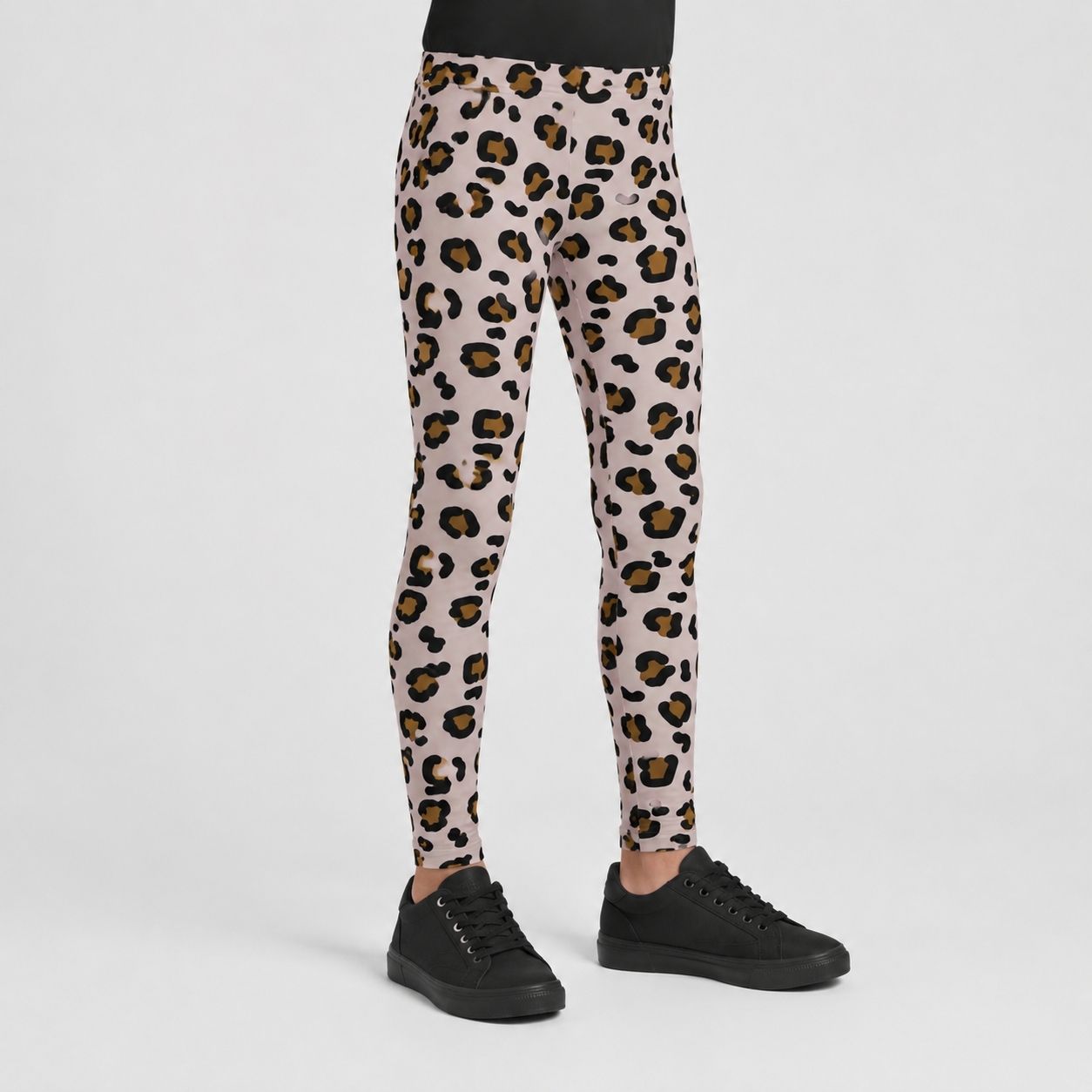 A person shown from the waist down wearing leopard-print leggings with black sneakers, photographed against a clean light gray studio background.