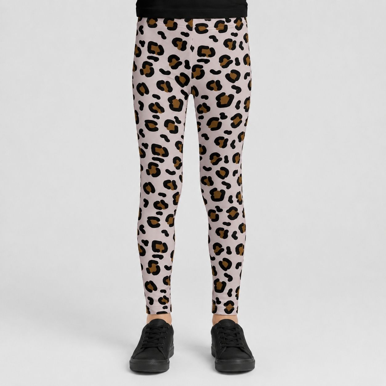 A person wearing leopard-print leggings with black sneakers, shown from the waist down against a light gray studio background.