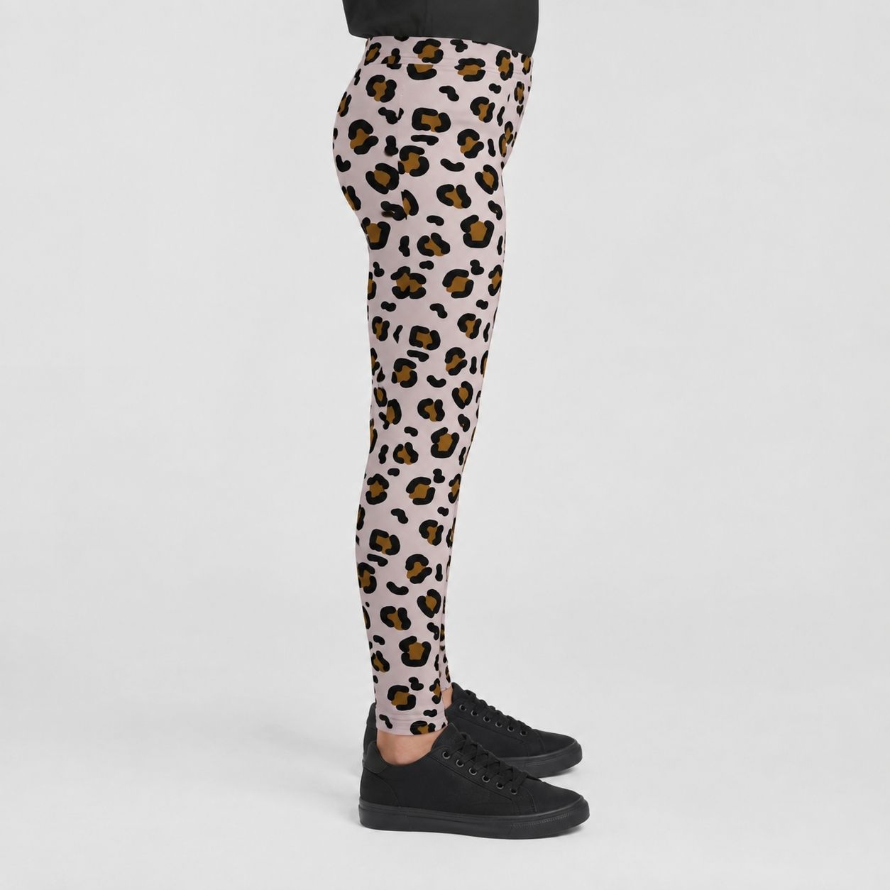 A person shown from the waist down wearing leopard-print leggings and black sneakers against a light gray studio background.