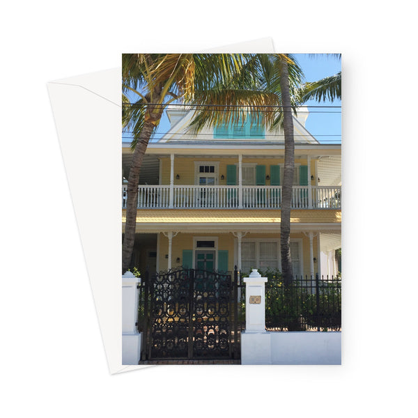 This greeting card shows a traditional conch house beneath palm trees with yellow walls, white veranda and turquoise shutters .