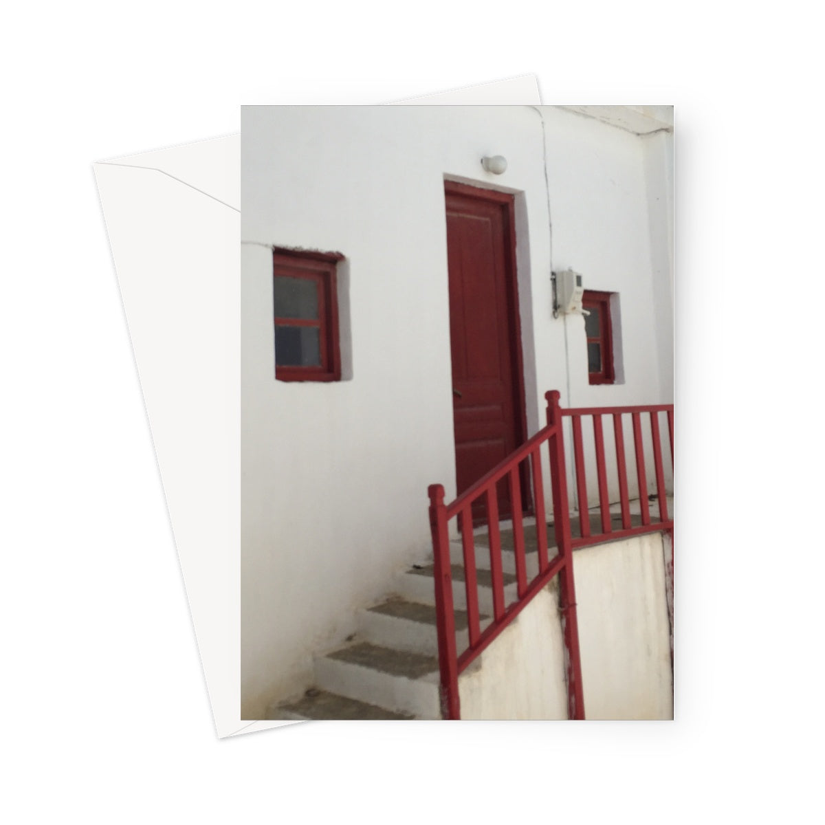 Greeting card showing red staircase against a traditional whitewashed Greek house. There is a red door and two small red windows.