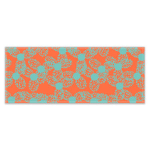 The patterned table runner has an abstract floral pattern in a taupe or turquoise dotted outline against an orange background