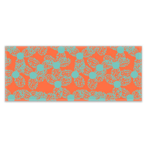 The patterned table runner has an abstract floral pattern in a taupe or turquoise dotted outline against an orange background