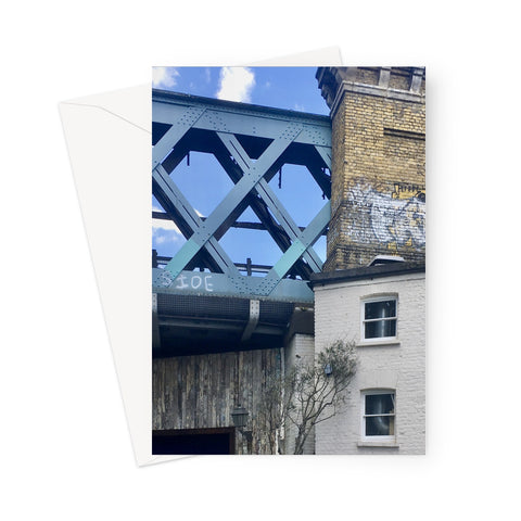 Blue cast iron railway bridge runs behind and above a nineteenth century white-painted building, with graffiti sprayed onto some of the old brickwork in this greeting card