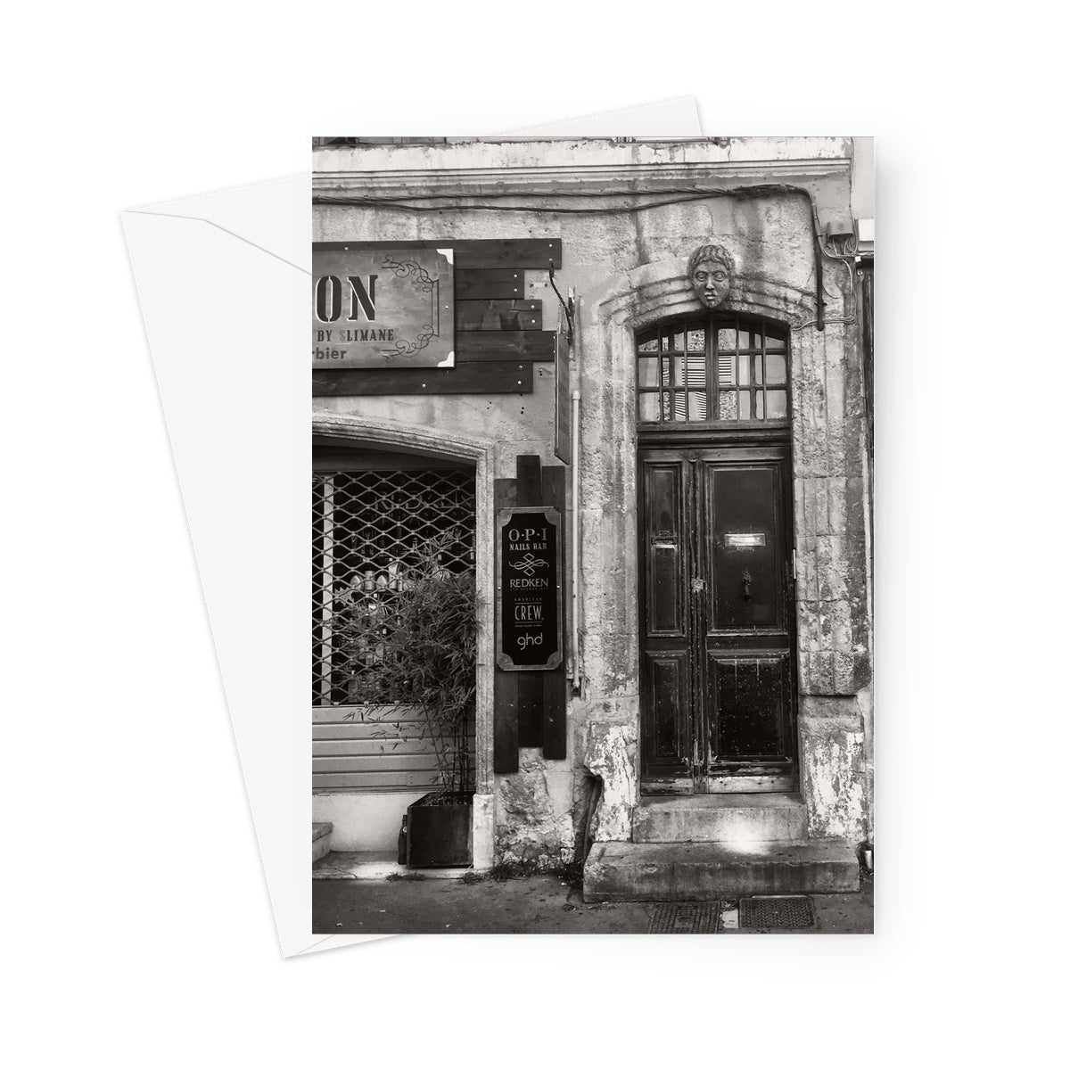 Greeting card showing old doorway on the right in black and white. Carved head is positioned over the top of the doorway. A shop is shown partially to the left.