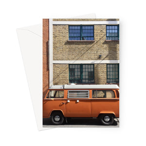 Greeting card showing an orange retro campervan parked in front of a lovely early 20th century building