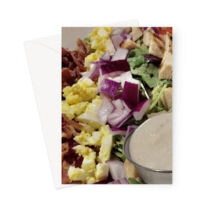 Closeup of a cobb salad, containing bacon bits, chopped egg, red onions, lettuce, chicken cubes and tomato in this greeting card. A portion of blue cheese sauce sits in the bottom right corner.