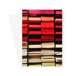 A shelf of coloured sheets of paper ranging from pink, red to yellow and white in this photo greeting card