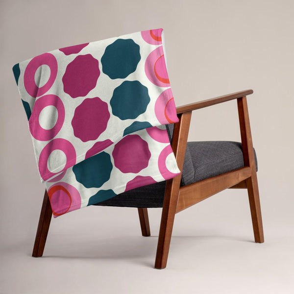 This Mid-Century Modern style couch throw consists of colorful circular and concentric shapes in various tones of pink and top against a light cream background