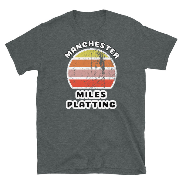Distressed style abstract retro sunset graphic in yellow, orange, pink and scarlet stripes. The name of Manchester is displayed at the top wrapped around the sunset. Below the retro sunset design is the famous Manchester place name of Miles Platting on this dark grey cotton t-shirt.