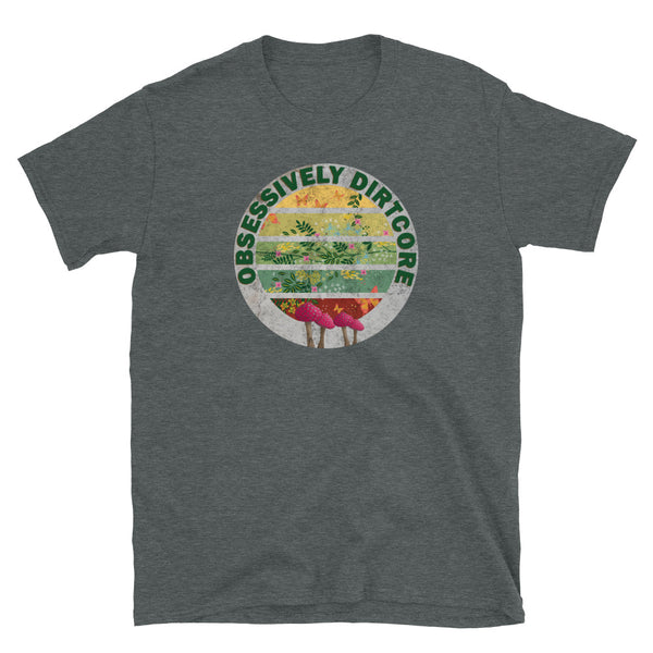 Circular design on this t-shirt with an inner vintage sunset style circular shape containing a gradient colour of crimson, teal, green, mustard and ochre and a cute pattern of orange butterflies, green leaves, pink flowers in a Cottagecore aesthetic. Around the upper edge of this design are the words in bold olive green font Obsessively Dirtcore. At the base of this design there are four fly agaric mushrooms. Dark heather tee by BillingtonPix
