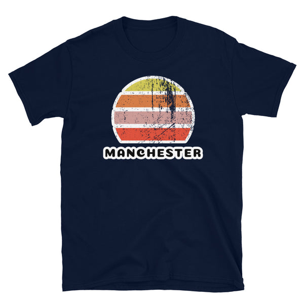 Features a distressed abstract retro sunset graphic in yellow, orange, pink and scarlet stripes rising up from the famous Manchester place name on this navy t-shirt