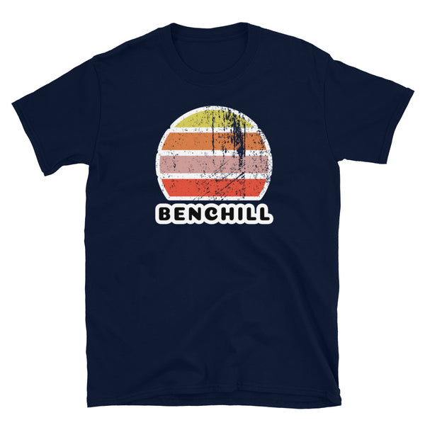 Distressed style abstract retro sunset graphic in yellow, orange, pink and scarlet stripes above the famous Manchester place name of Benchill on this navy cotton t-shirt