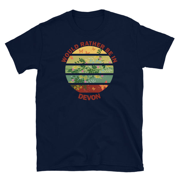 Cottagecore style floral and butterfly design within a Vintage Sunset abstract shape in tones of crimson, teal, green, mustard and yellow stripes with the slogan Would Rather Be in Devon on this navy cotton t-shirt by BillingtonPix