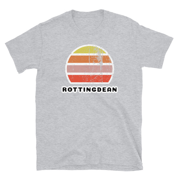 Distressed style abstract retro sunset graphic in yellow, orange, pink and scarlet stripes rising up from the famous Brighton place name of Rottingdean on this sport grey  t-shirt