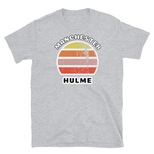 Distressed style abstract retro sunset graphic in yellow, orange, pink and scarlet stripes. The name of Manchester is displayed at the top wrapped around the sunset. Below the retro sunset design is the famous Manchester place name of Hulme on this light grey cotton t-shirt.