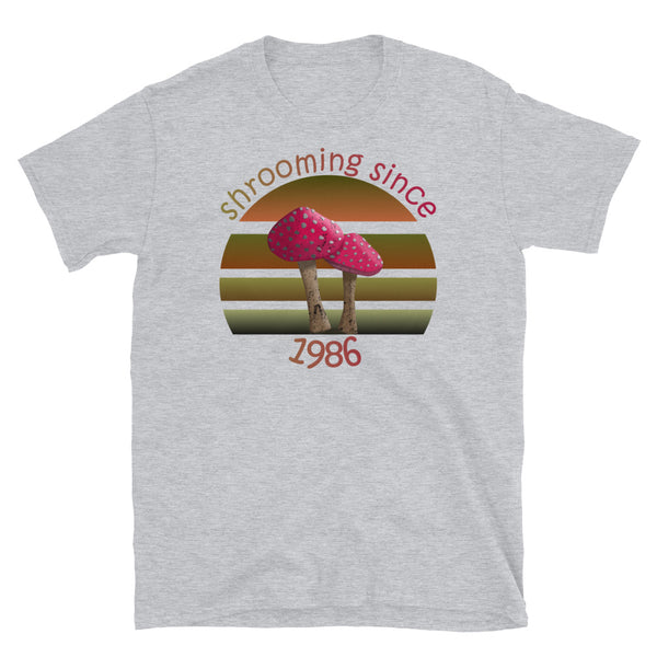 Shrooming since 1986 cute Goblincore style design with two red fly agaric mushrooms with distressed look against a multi-toned nature colour palette abstract vintage sunset design on this sport grey cotton t-shirt by BillingtonPix